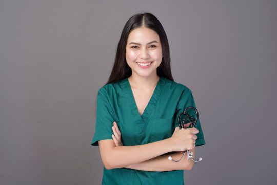 a female doctor wearing a green scrubs and stethoscope is on grey background studio